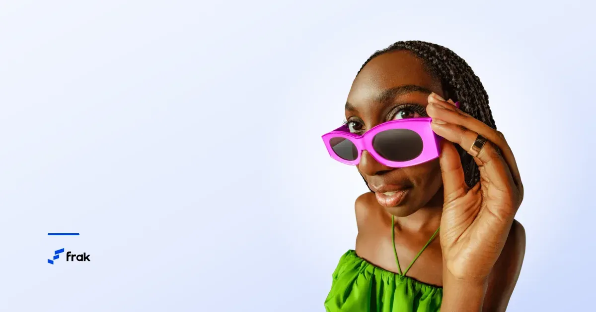 A woman lowering her pink sunglasses to look straight at the camera, against a pale blue background.